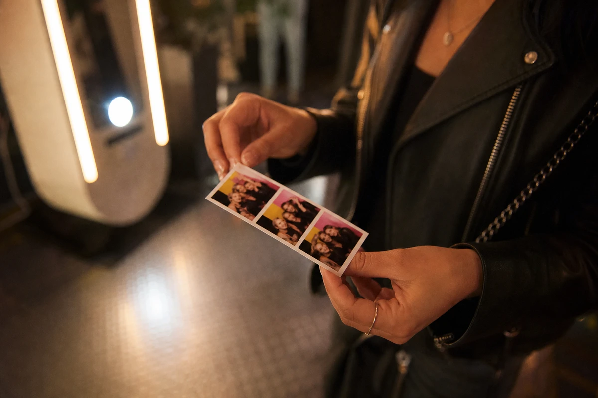 A guest's hands hold a freshly printed photo strip just received from a venue photo booth, the small photos soft and abstracted.