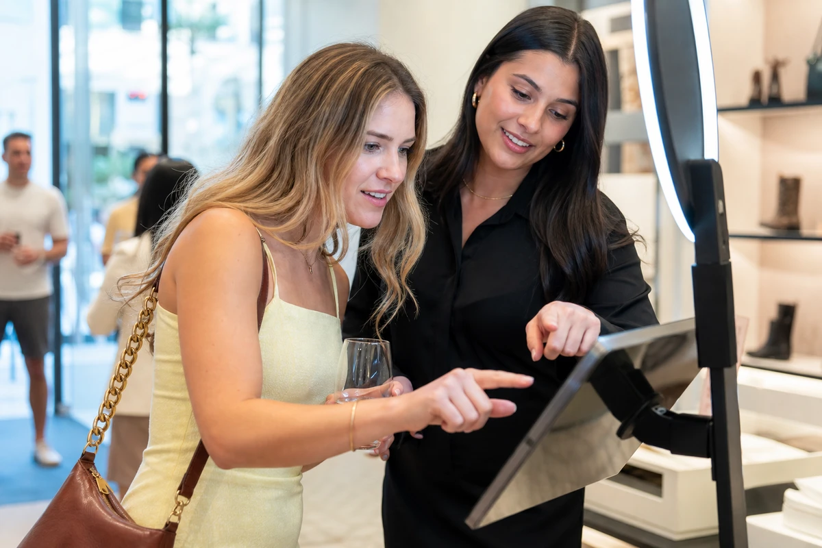 A guest entering her name and email on a photo-booth tablet while a host points helpfully, turning an anonymous visitor into a known contact.