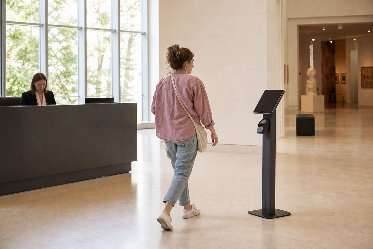 A self-service membership kiosk stands a few feet beside a museum admissions desk as a visitor steps toward it.