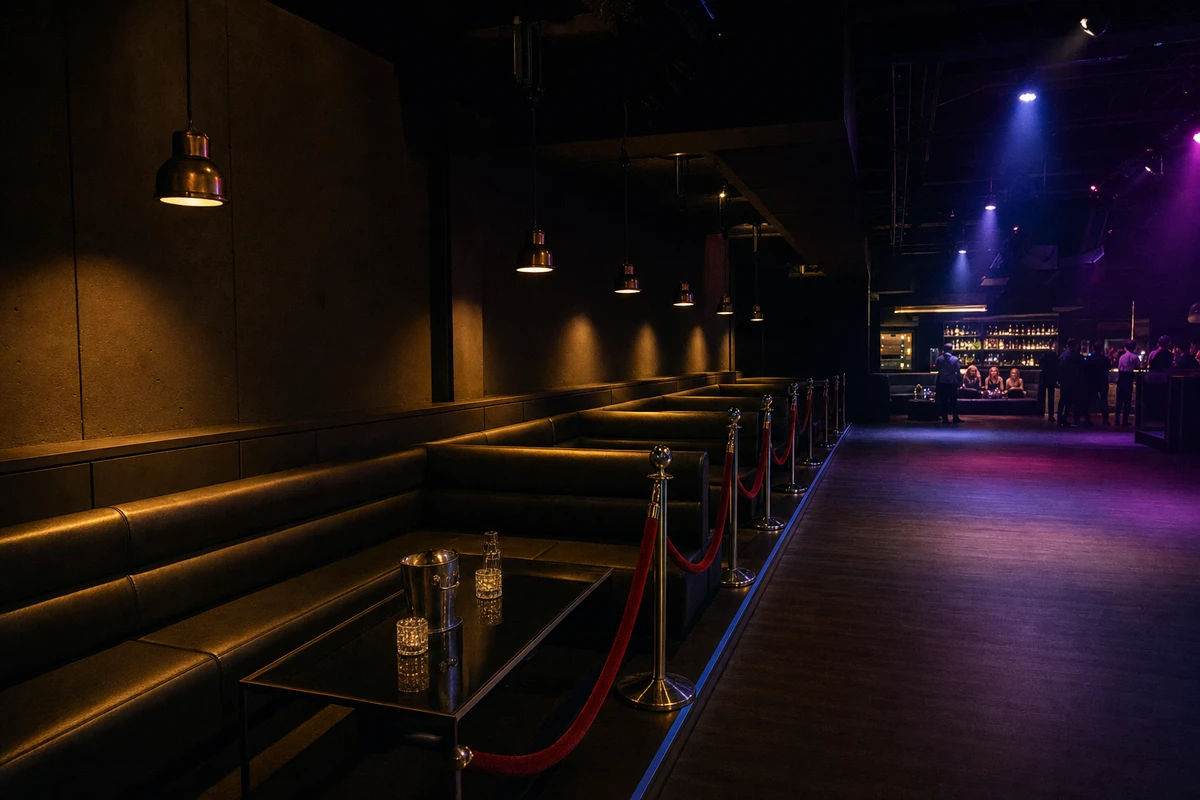 A row of empty, velvet-roped VIP banquettes sits lit but unoccupied along the wall of a nearly empty nightclub early in the night.