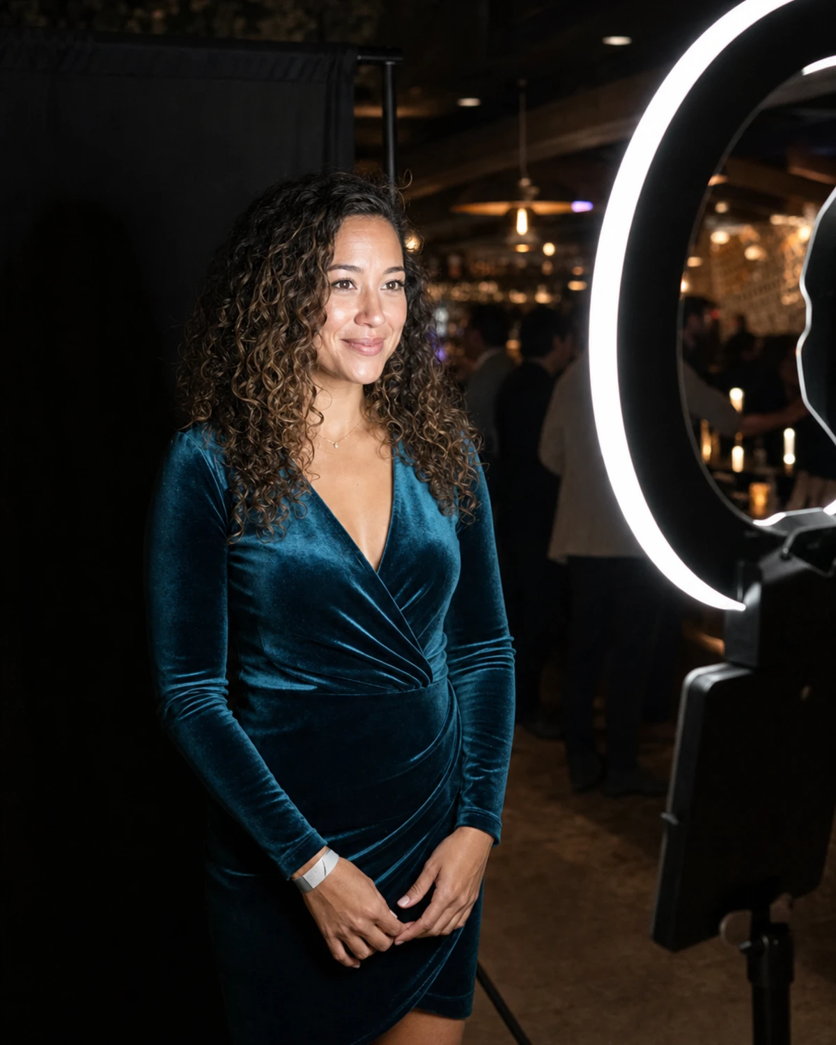 A single guest's face is evenly and cleanly lit by the white circular ring light of an open-air photo booth in an otherwise dim lounge venue.