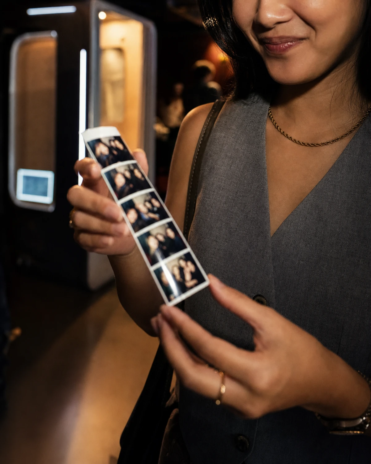 A guest holds a freshly printed photo strip from a photo booth, smiling as they look at the captured keepsake.