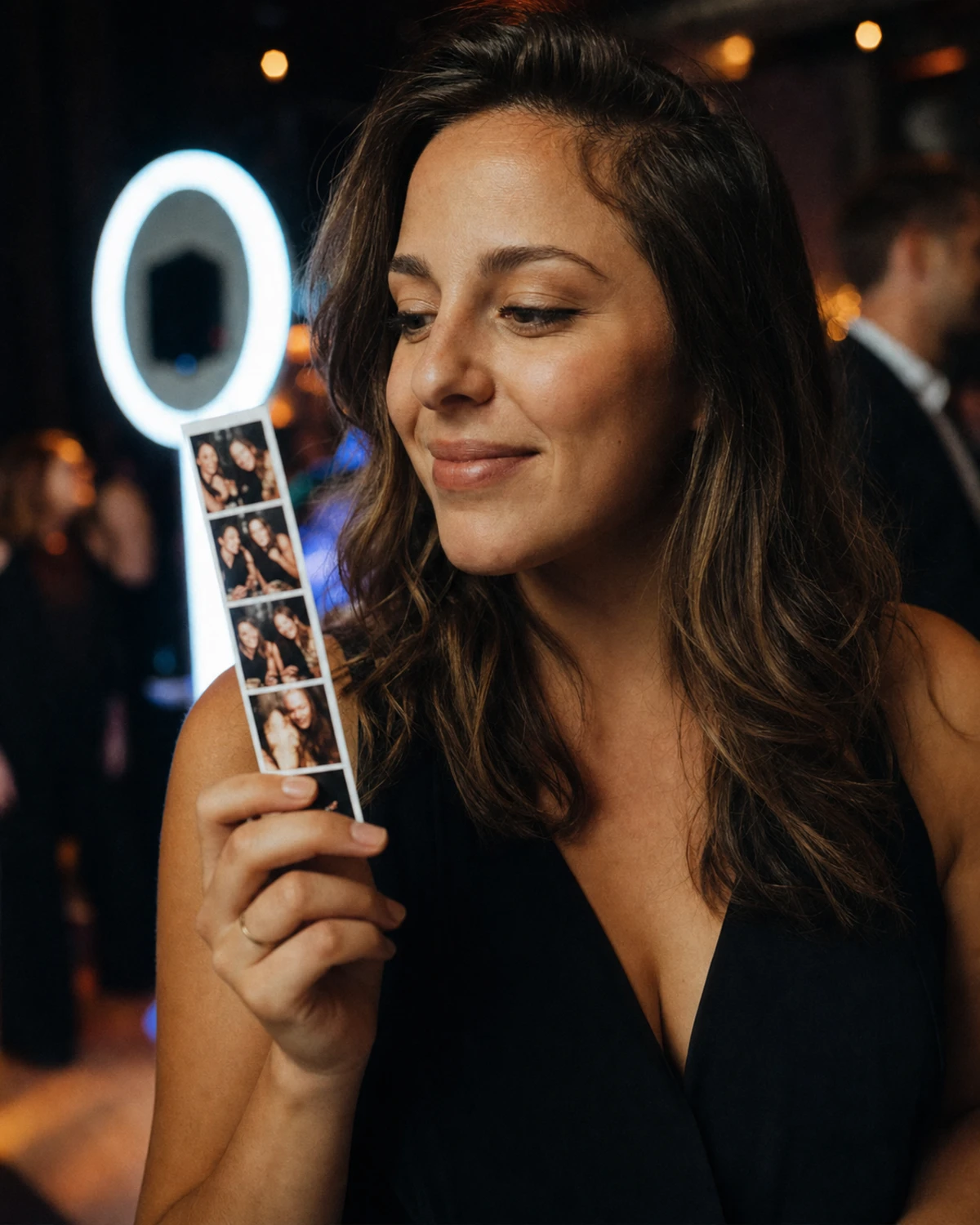 A guest studying a freshly printed photo strip with a pleased smile just after a photo-booth session, deciding whether to share it.