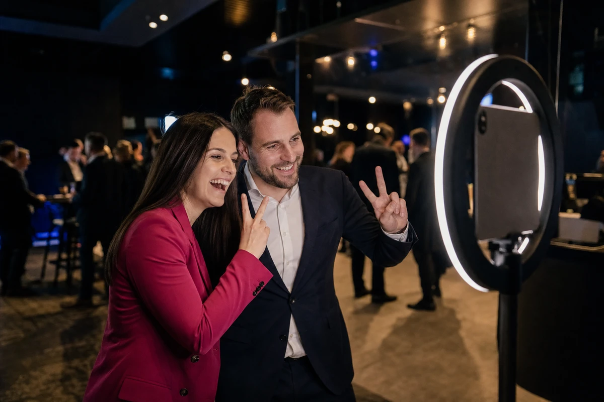 Two professional conference attendees posing together mid-session at an iPad photo booth in a dark upscale event venue, the booth screen turned away from the camera.