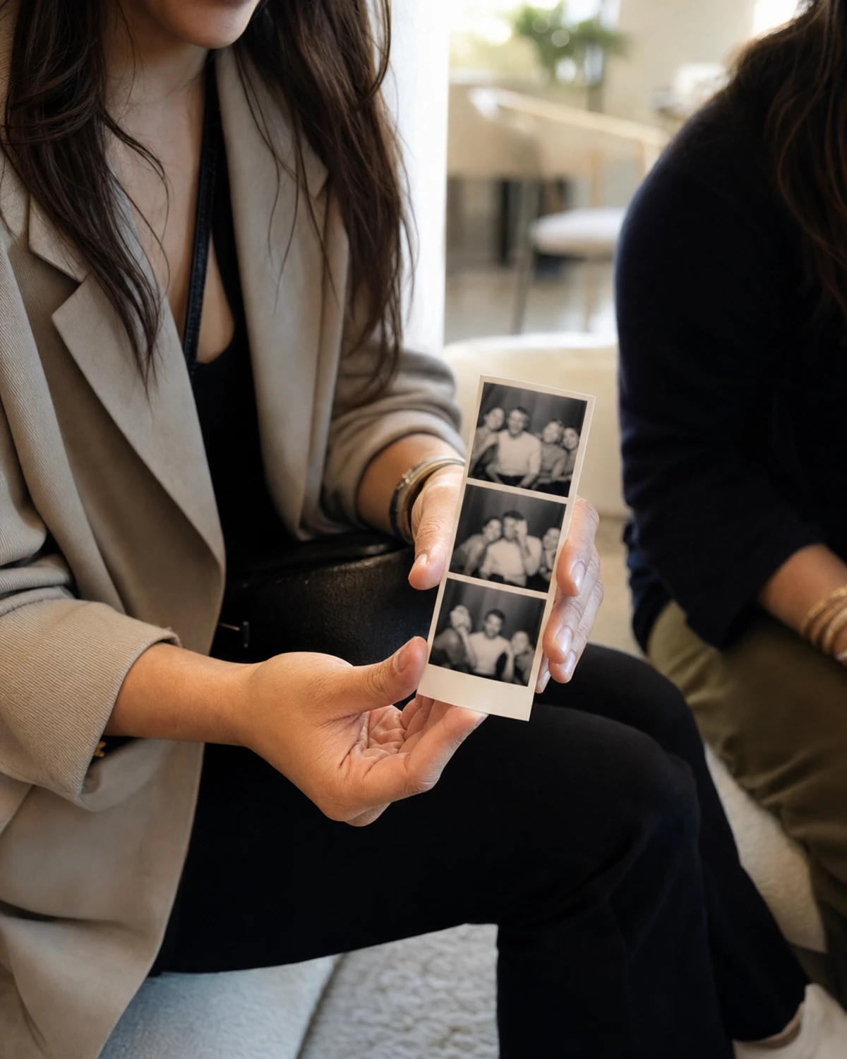 A venue guest's hands holding a freshly printed photo strip received from a photo booth at a corporate activation, the small frames soft and gestural.