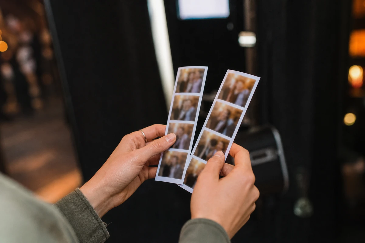 A guest holds two freshly printed photo strips in both hands just after a photo booth session, the venue glowing softly out of focus behind.