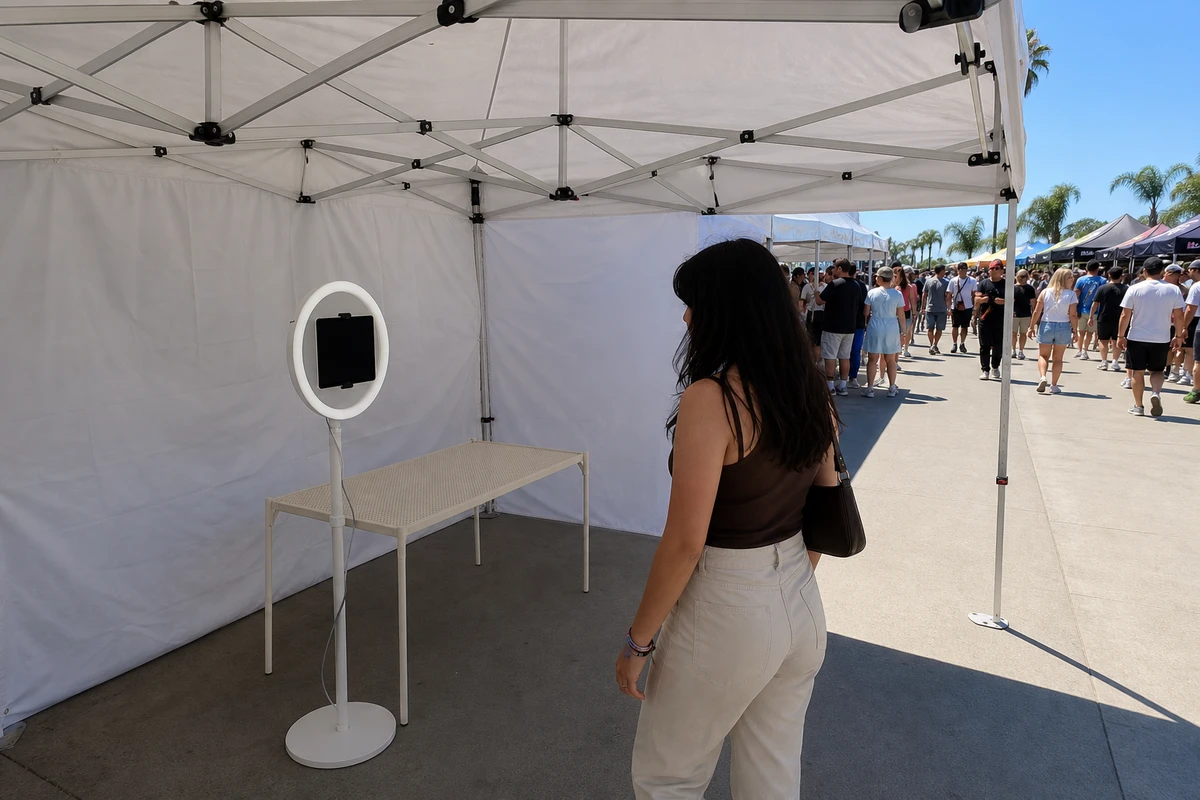 An iPad photo booth set up under a plain white event canopy, shaded from the bright sun, with clear floor space around it.