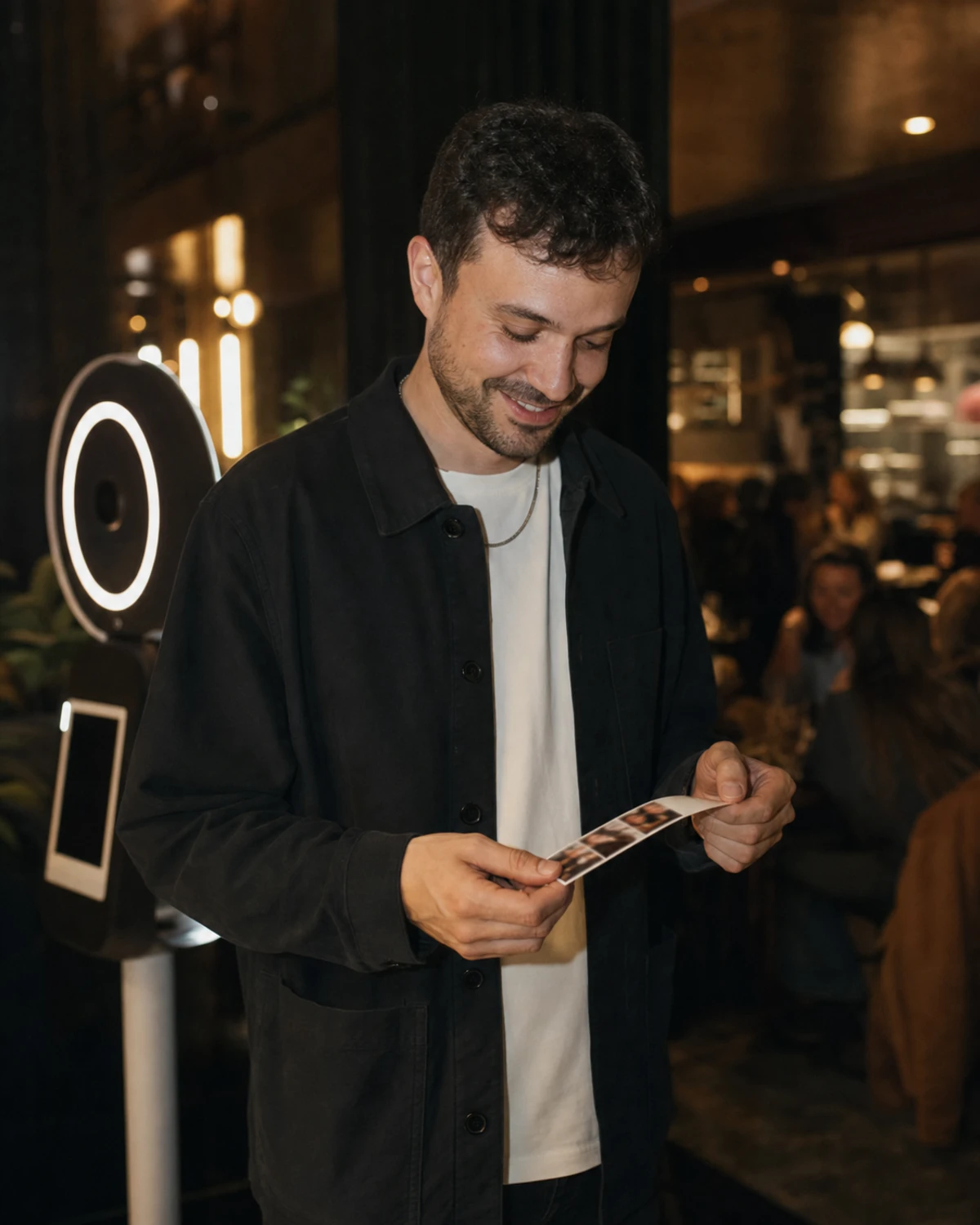 A restaurant guest smiles while looking at a freshly printed photo strip he received from an in-venue photo booth.