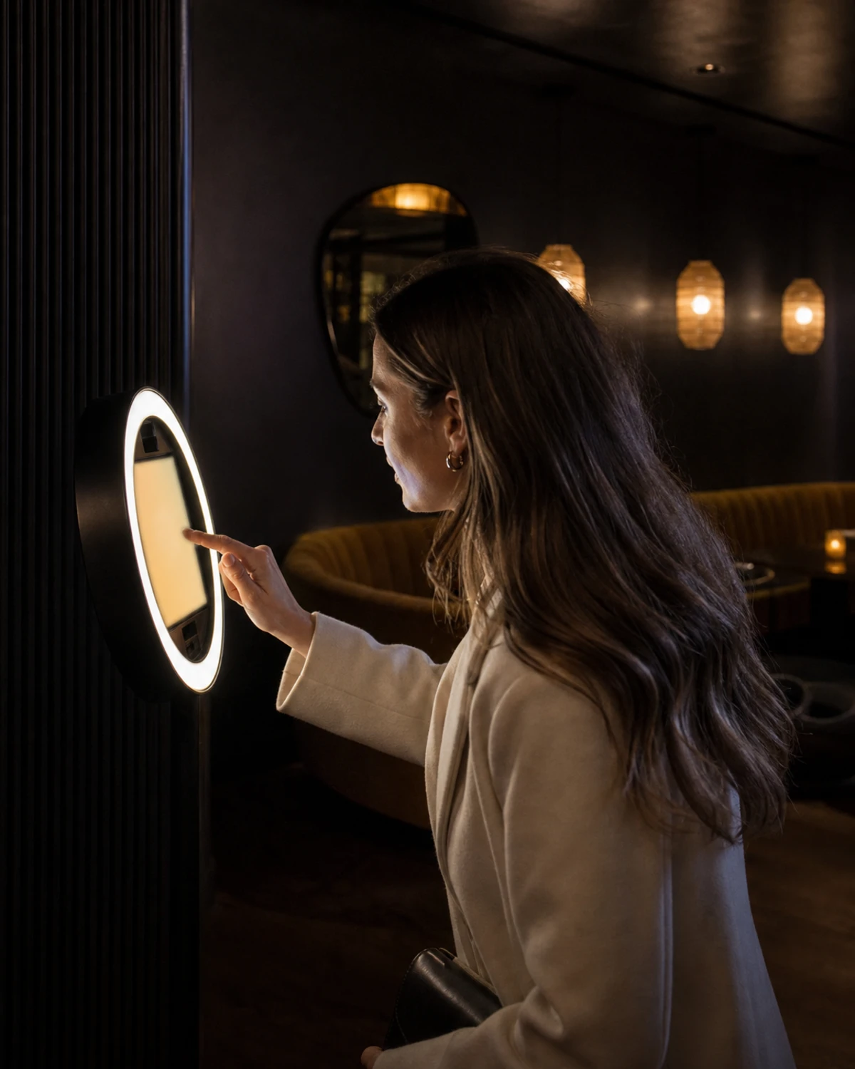 A restaurant guest reaching toward the screen of an iPad photo booth in a dim lounge corner to enter her contact details