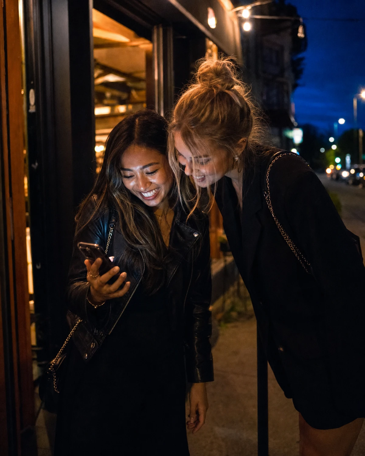 Two restaurant guests standing outside the entrance, smiling at a phone showing the branded photo the booth just sent them