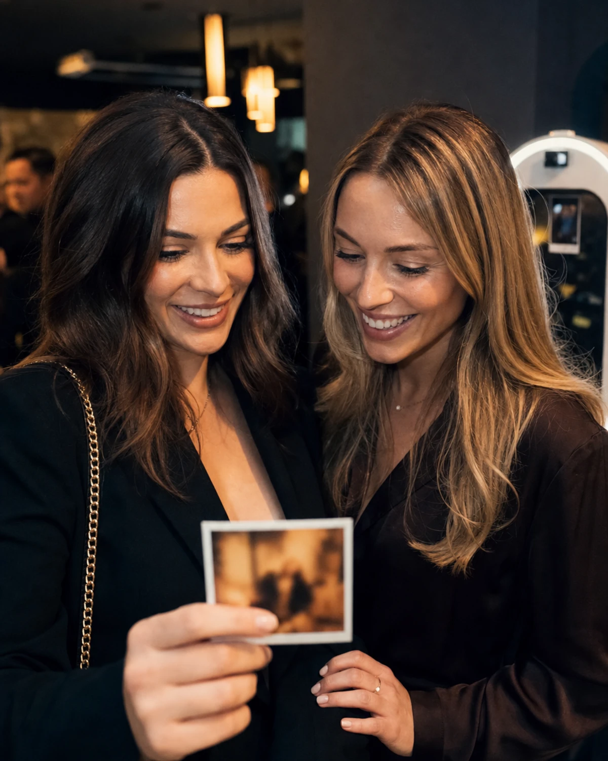 A med spa patient showing a freshly printed photo to a friend beside her during a VIP client night, both smiling at the small print.