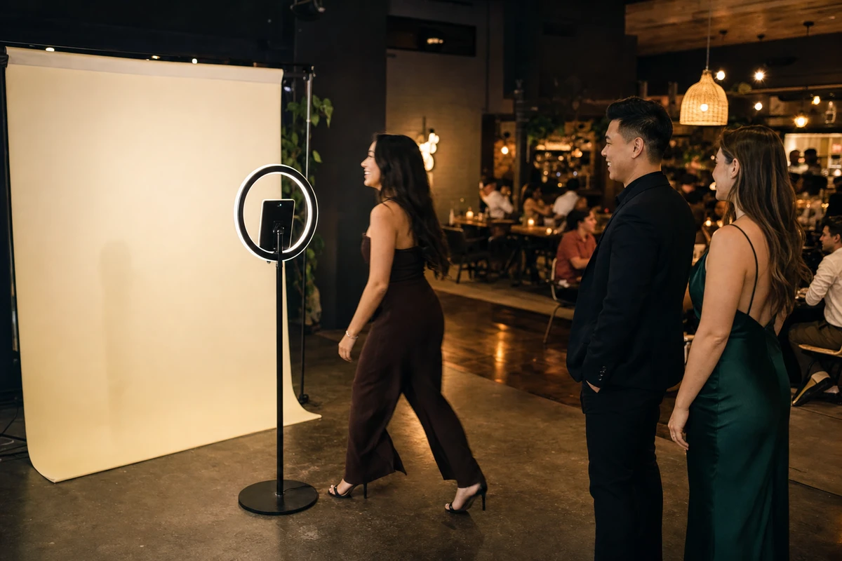 Side view of guests using an open-air iPad photo booth at a venue, one stepping in to start a session as two others wait nearby.