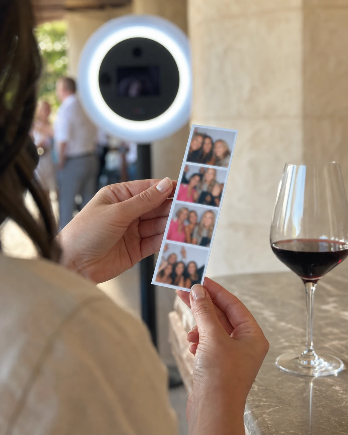 A winery guest's hands holding a freshly printed branded photo strip collected from the tasting-room photo booth.
